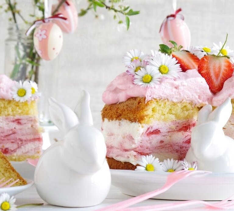 Erdbeertorte mit Biskuitboden und Gänseblümchen / Ostertafel / zwei Deko-Hasen aus Porzellan / Vase mit verzierten Ostereieren | © Shutterstock / Bildagentur Zoonar GmbH