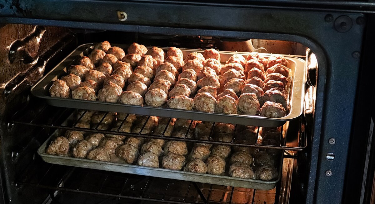 Frikadellen im Backofen zubereiten / zwei Bleche mit Hackbällchen / Draufsicht, schräg
