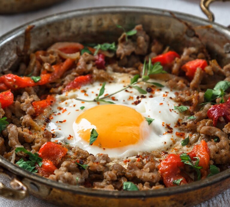 Kiymali Yemek mit Spiegelei und frischen Kräutern in einer runden Pfanne aus Metall / Gabel / Untergrund Holz | © Shutterstock / Konstantin Kopachinsky