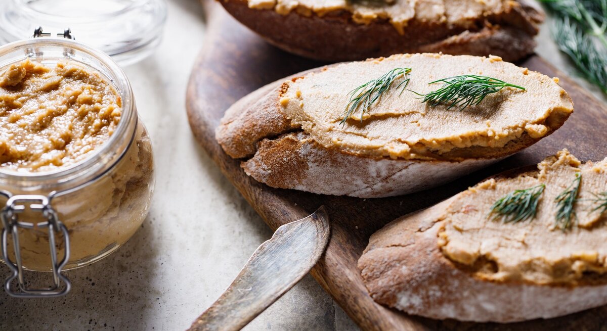 Thunfischcreme mit Dill auf zwei Weißbroten / Messer / Dip im Glas / Messer / Holzbrettchen