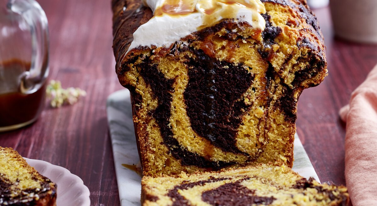Kürbis-Kakao-Kuchen auf einem grauen Servierteller, auf dunkelrotem Hintergrund. 