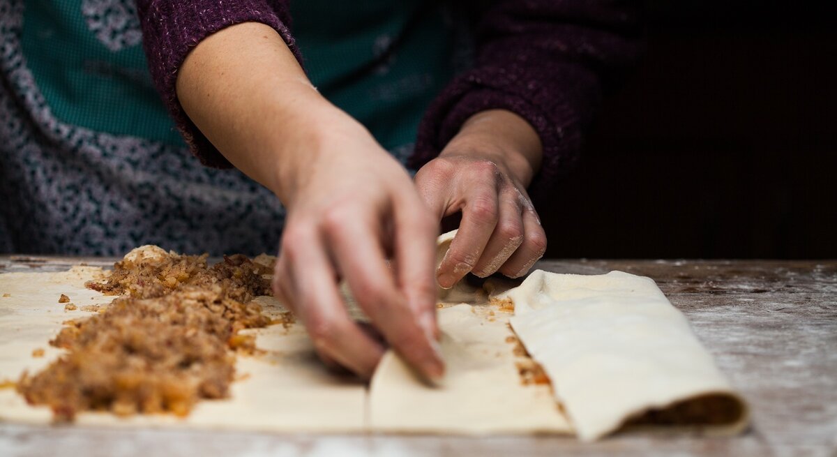 Strudelteig selbst machen / vorbereitete Apfelfüllung / zwei Hände einer Frau / bemehlte Arbeitsfläche aus Holz / Frontale Sicht