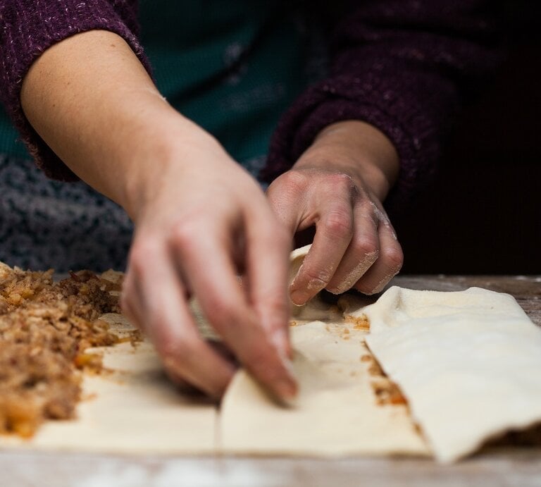Strudelteig selbst machen / vorbereitete Apfelfüllung / zwei Hände einer Frau / bemehlte Arbeitsfläche aus Holz / Frontale Sicht | © Shutterstock / Cryptographer