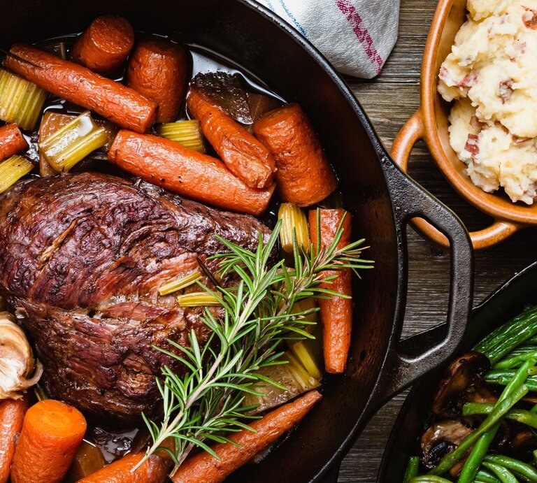 Brasato al Barolo, ein Schmorbraten aus Rindfleisch, in einem in einem gusseisernen Topf mit Griffen / Drumherum und ebenfalls im Topf Gemüse und Kräuter | © © Getty Images / Nadia Nice
