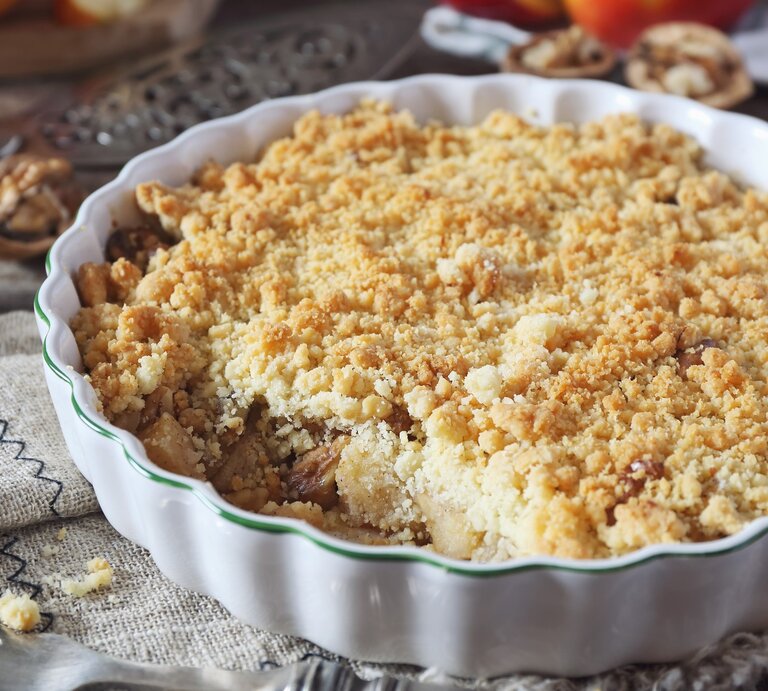Apfelkuchen mit Streusel und Walnüssen in runder Form / Apfelschnitten, frisch Walnüsse, Gabel | © Getty Images / Yulia Vinogradova