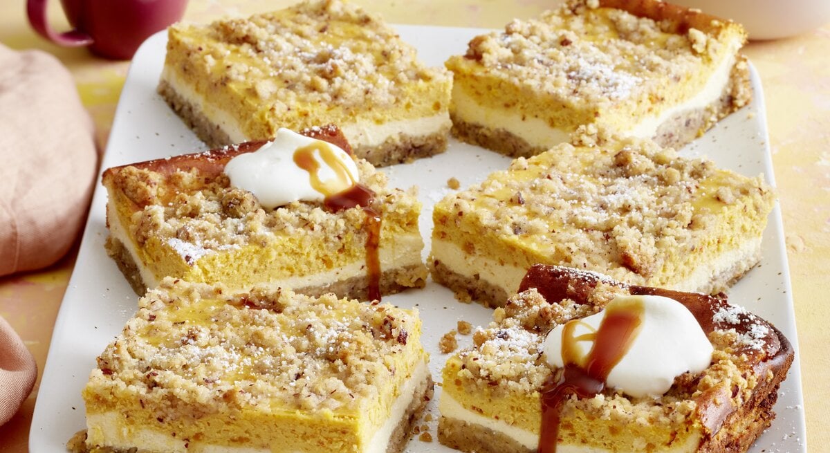 Draufsicht auf sieben Stücke des Kürbis-Streuselkuchen auf einer Kaffeetafel.