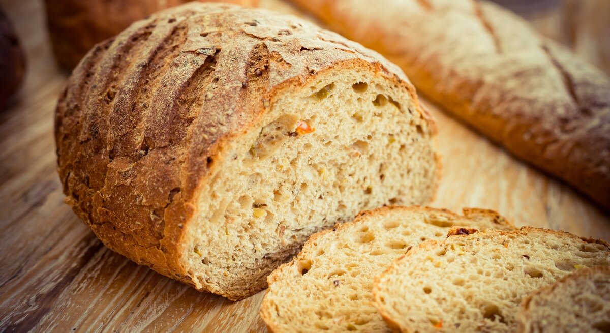 Ein Ezekiel-Brot / Angeschnitten / zwei Scheiben / Hintergrund: ein längliches Brot / Untergrund Holz