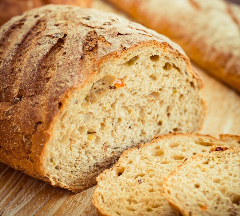 Ein Ezekiel-Brot / Angeschnitten / zwei Scheiben / Hintergrund: ein längliches Brot / Untergrund Holz | © Shutterstock / Pixx Media