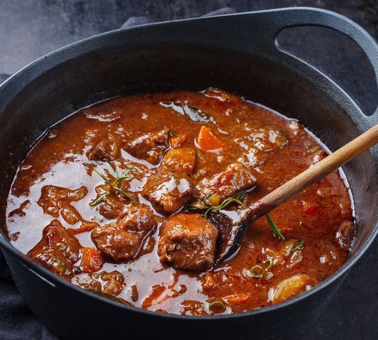 Ungarisches Gulasch wie bei Oma / Fleischstücke, Rosmarin, Möhrenstück / Holzlöffel im Topf / Draufsicht, schräg | © Adobe Stock / H.LEITNER