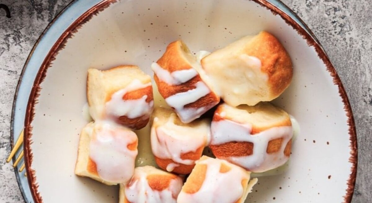 Vegane Buchteln mit Aprikosenmarmelade und Vanillesauce in einer Schüssel auf grauem Untergrund.