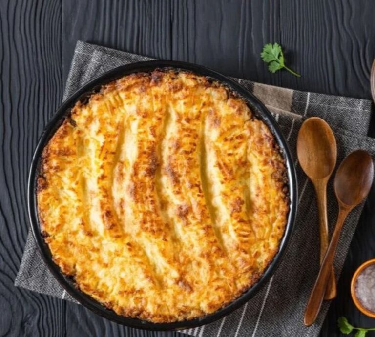 Veganer Linsen-Gemüse-Auflauf in runder Auflaufform auf dunklem Holztisch mit Linsen und Kräutern. | © Getty Images / from_my_point_of_view