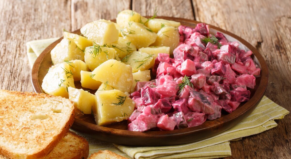 Roter Heringssalat, gekochte Kartoffeln, Dill auf runden Teller / zwei Scheiben Brot / Küchentuch / Untergrung grobes Holz / Draufsicht, schräg