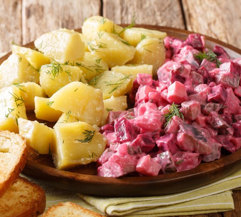 Roter Heringssalat, gekochte Kartoffeln, Dill auf runden Teller / zwei Scheiben Brot / Küchentuch / Untergrung grobes Holz / Draufsicht, schräg | © Adobe Stock / FomaA