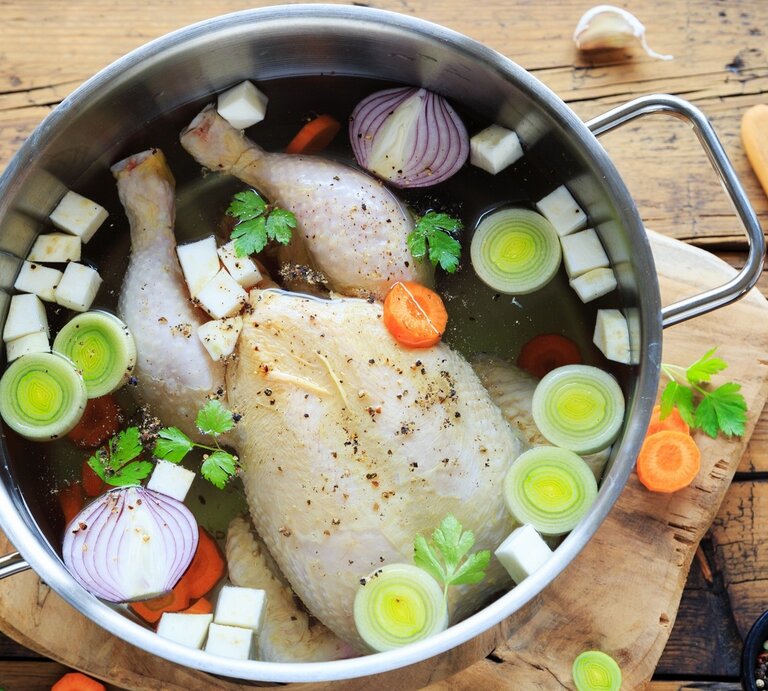 Hühnerbrühe im Topf / ganzen Suppenhuhn, klein geschnittenes Gemüse / Unterlagen Holzbrett auf Holzboden / frischer Pfeffer in Mörser / Holzlöffel / frisches geschnittenes Gemüse - Möhren, Knoblauch, Sellerie, Petersilie | © Shutterstock / juefraphoto