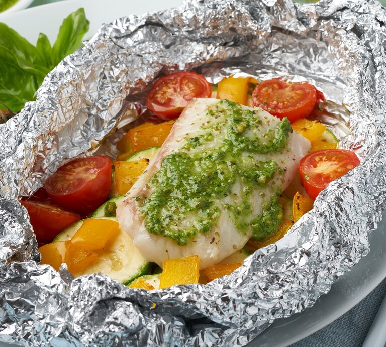 Fischfilet-Päckchen aus dem Ofen in Pesto bestrichen / In Alufolie gewickelt mit Tomaten, Paprika und Zucchini / Draufsicht schräg | © Shutterstock / Nata Bene