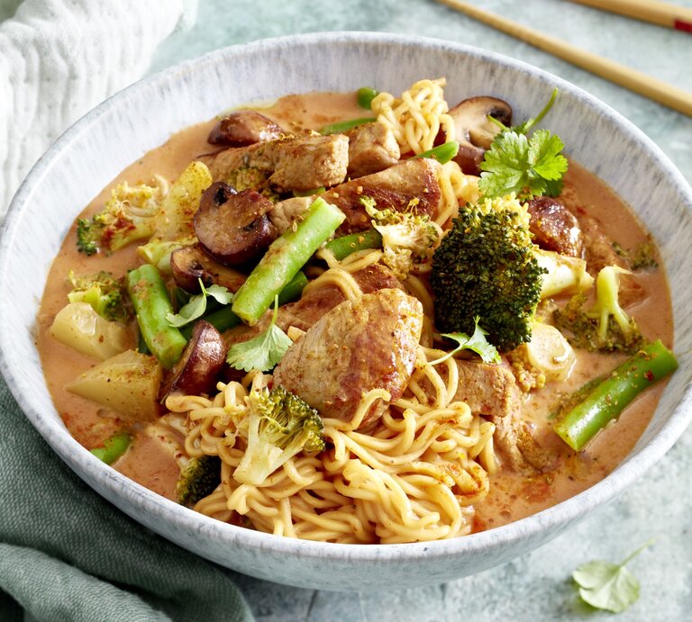 Thai-Curry mit Nudeln in einer hellgrauen Schüssel auf hellgrauem Hintergrund. Links ein Geschirrtuch, rechts Stäbchen.  | © Erlebe die Magie Thailands in einer Schüssel mit unseren aromatischen Thai-Curry-Nudeln - eine Reise für deine Geschmacksknospen, die du immer wieder erleben möchtest!