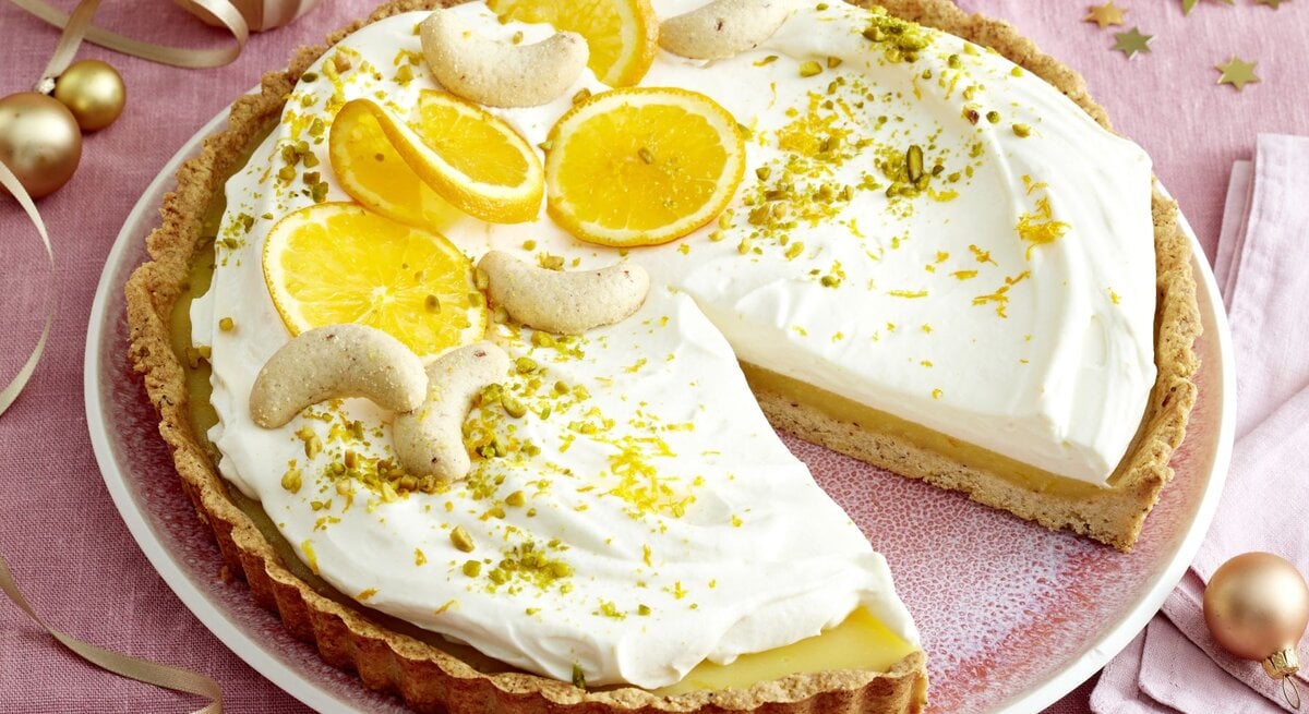 Orangen-Nuss-Tarte mit Sahnecreme, Orangenscheiben und Nüssen auf einer Tortenplatte.