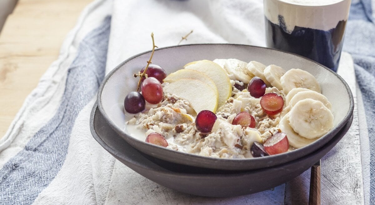 Bircher Müsli mit Haferflocken, Banane, Trauben und Apfelscheiben in einer Schale.