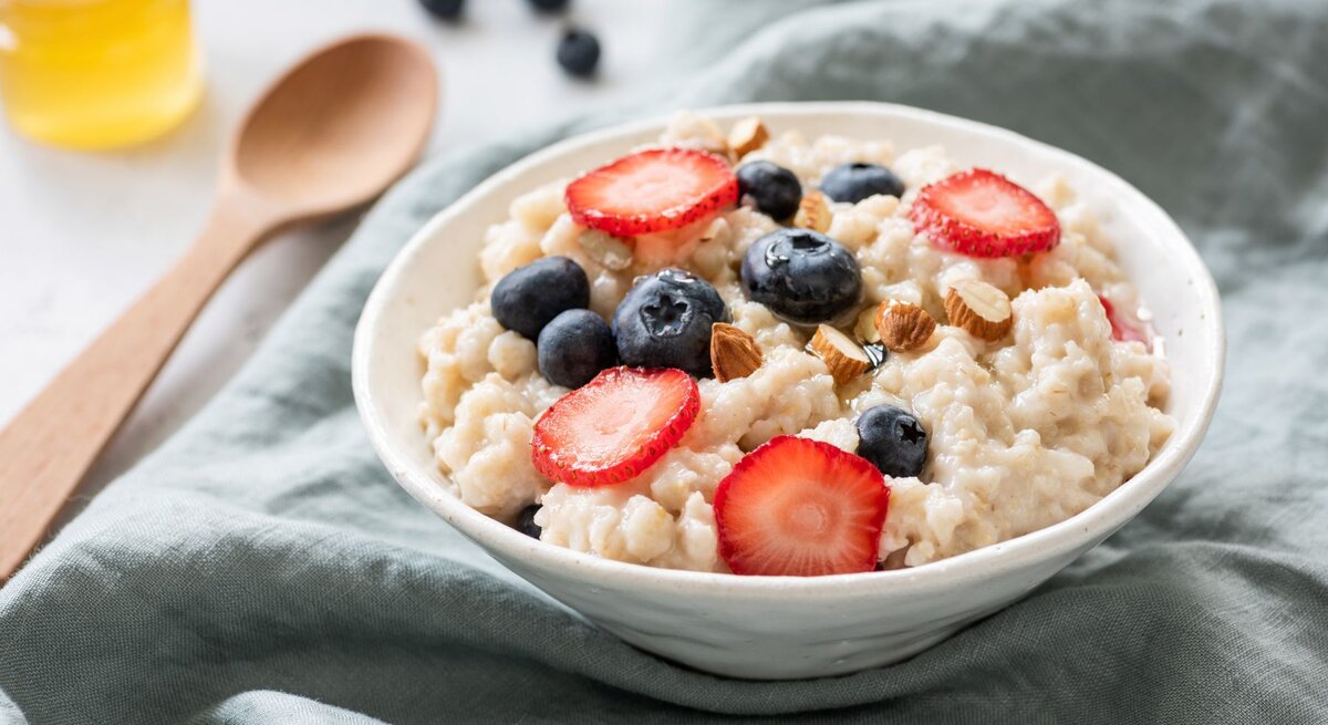 Cremiges Porridge in einer Schale mit Erdbeeren, Blaubeeren, Mandeln und Honig.