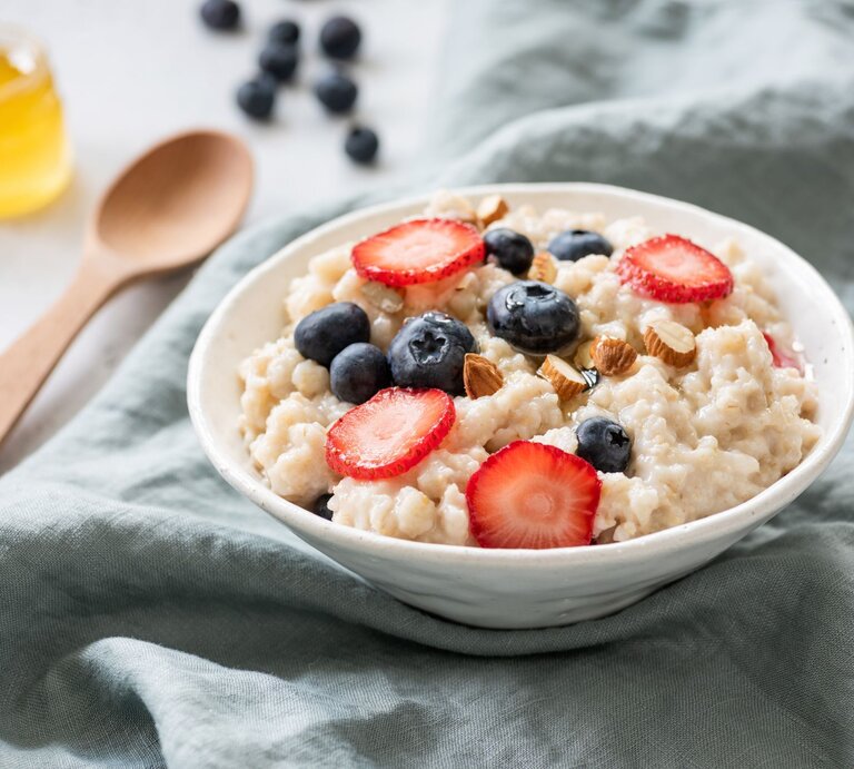 Cremiges Porridge in einer Schale mit Erdbeeren, Blaubeeren, Mandeln und Honig. | © GettyImages/	Arx0nt