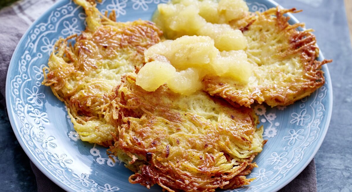Goldbraun gebratene Kartoffelpuffer auf einem Teller mit Apfelmus.