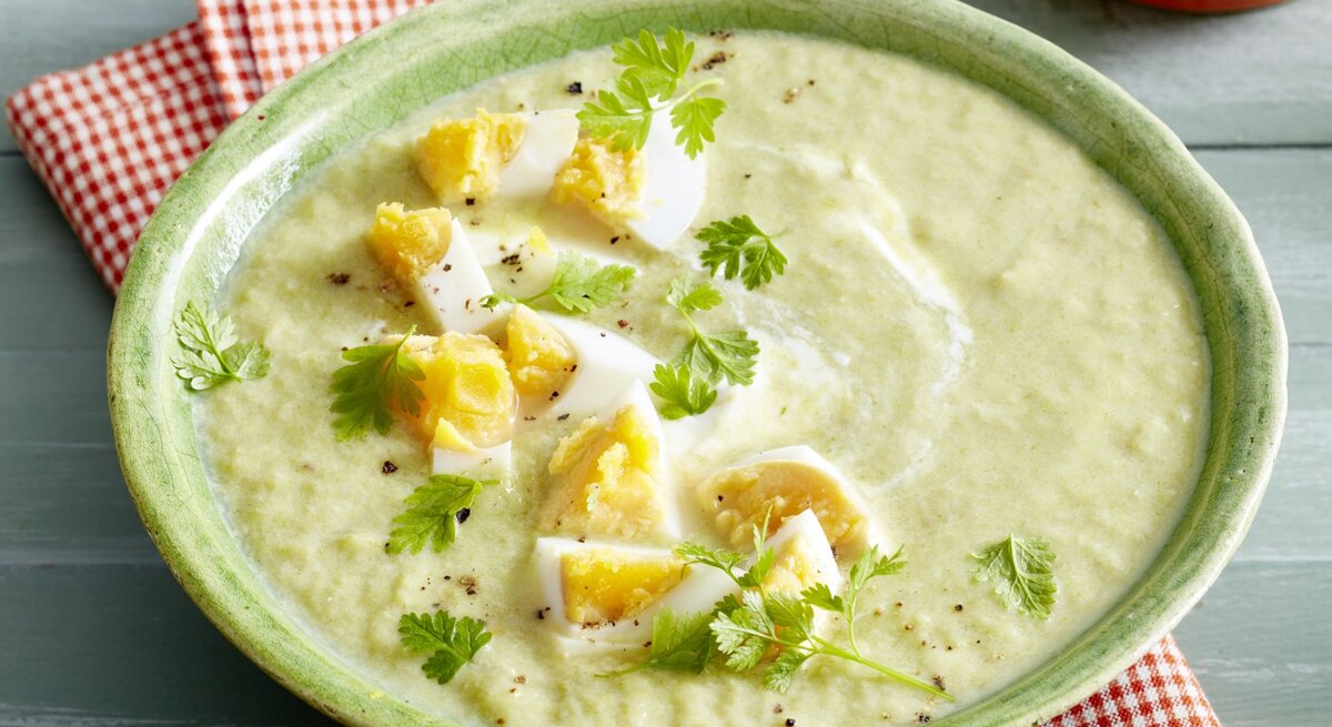 Eine Schale mit cremiger Lauch-Champignon-Suppe, verziert mit gehacktem hartgekochtem Ei und frischem Kerbel. Die Suppe hat eine hellgrüne Farbe mit weißen Joghurtwirbeln.