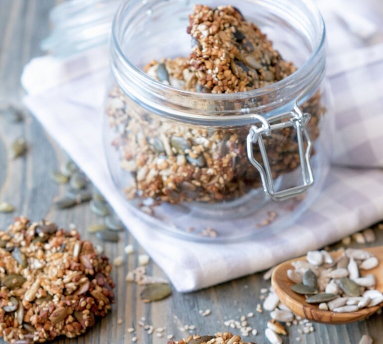 Low Carb Cracker mit Kernen in einem Schraubglas, daneben einige Cracker und verstreute Kerne auf einem Holztisch. | © EAT CLUB/Isabell Triemer