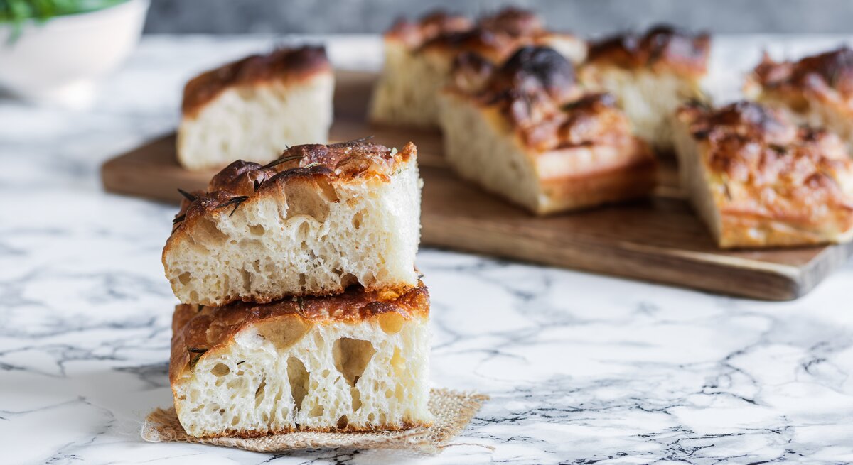 Nahaufnahme von zwei Stück fluffiger Focaccia, im Hintergrund weitere Focacciastücke.