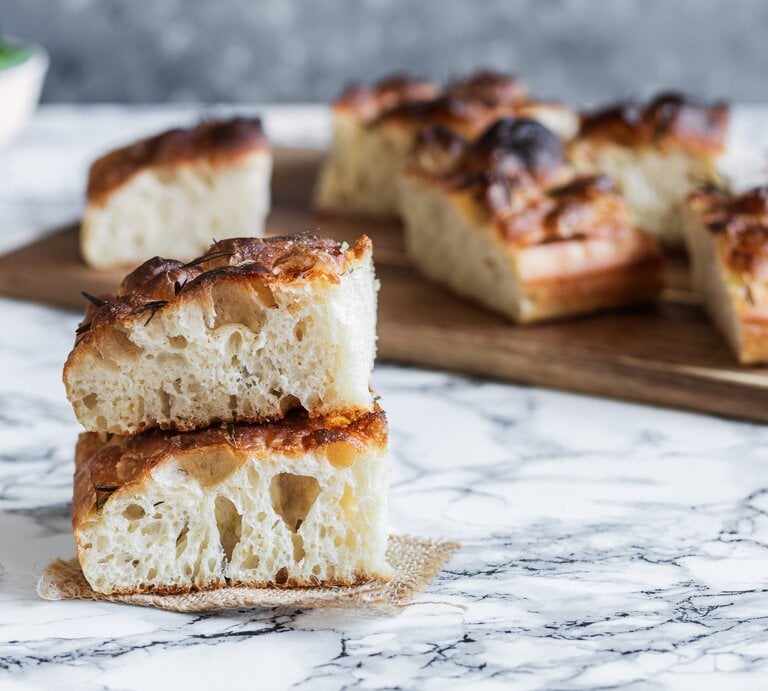 Nahaufnahme von zwei Stück fluffiger Focaccia, im Hintergrund weitere Focacciastücke. | © Getty Images / Ana Larrosa