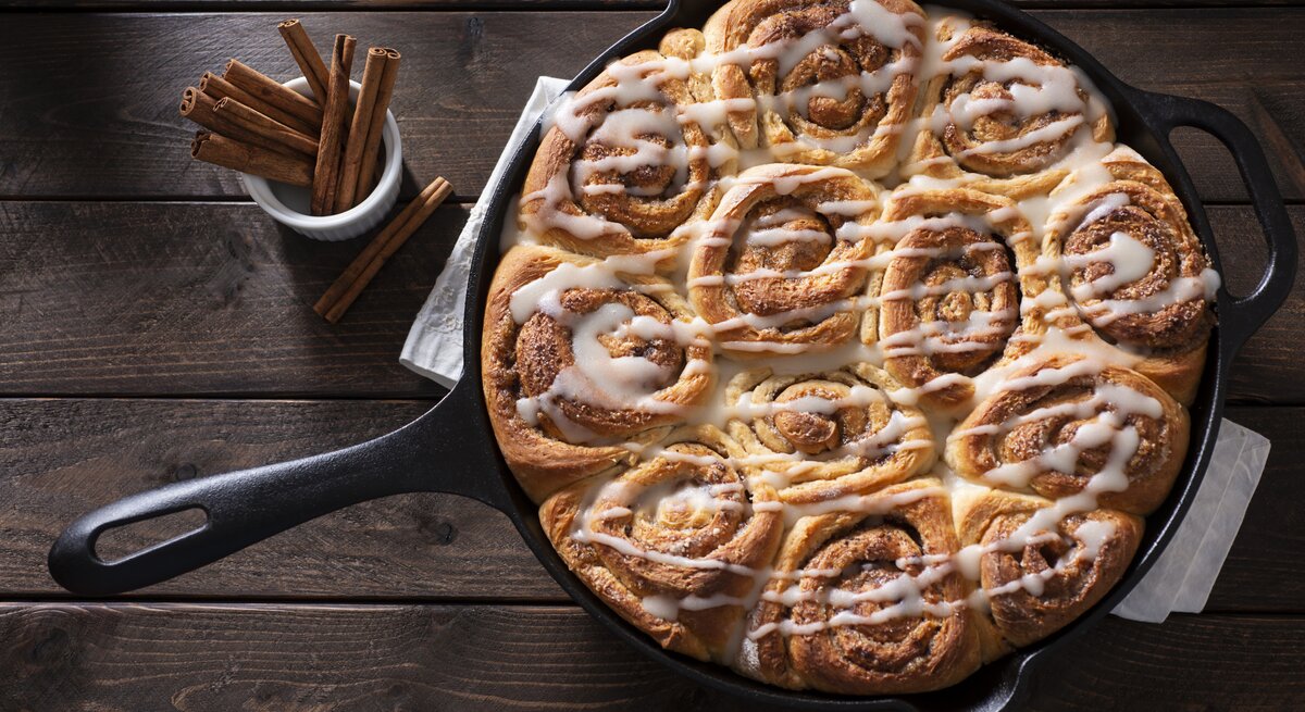 Draufsicht auf einer gusseiserne Pfanne mit saftigen Zimtschnecken, die mit einem Frischkäse-Frosting garniert sind.