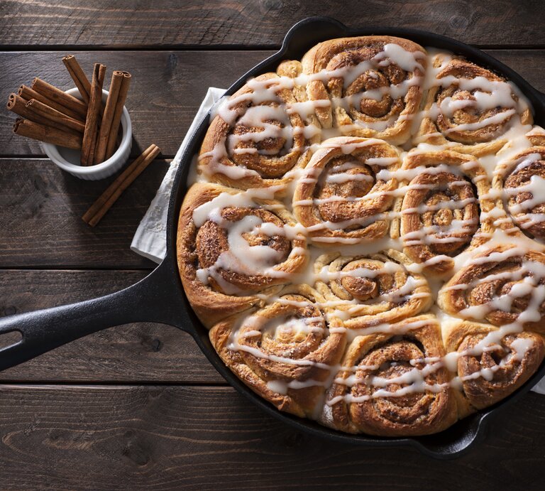 Draufsicht auf einer gusseiserne Pfanne mit saftigen Zimtschnecken, die mit einem Frischkäse-Frosting garniert sind. | © Getty Images / rudisill