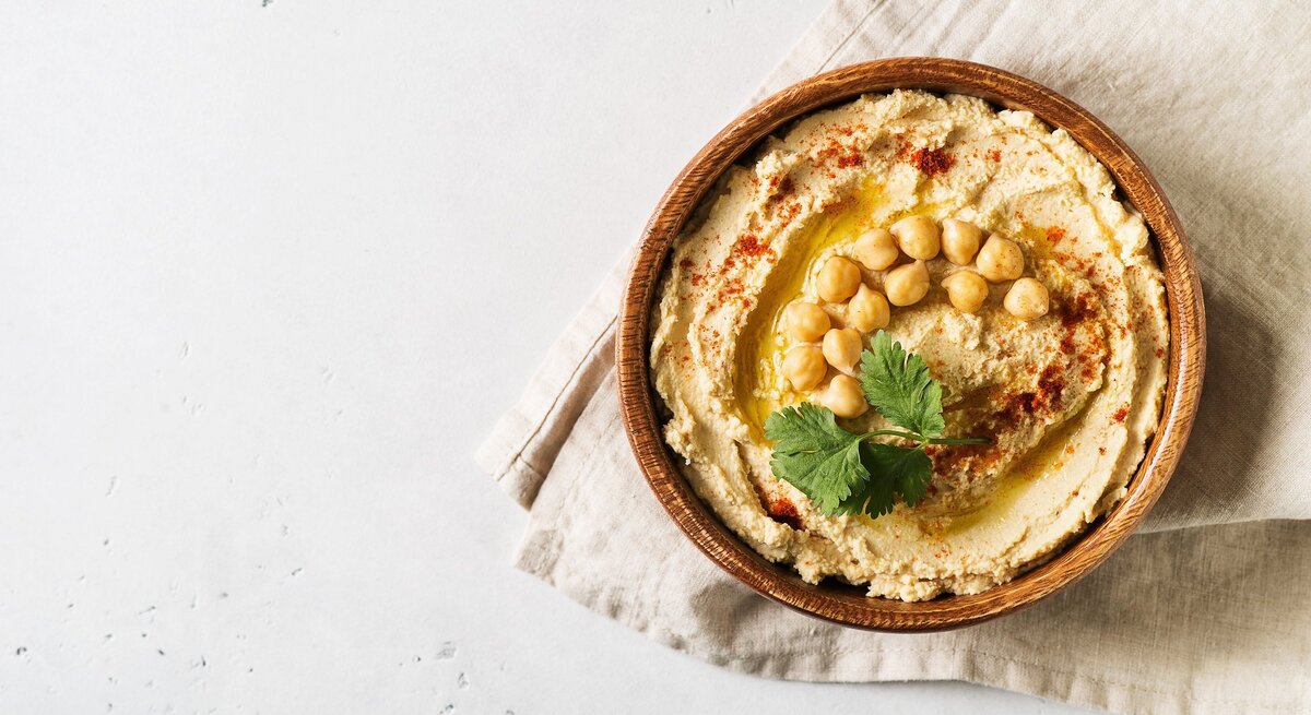 Klassischer Hummus und ganze Kichererbsen in einer runden Schüssel aus Ton / Handtuch / Draufsicht