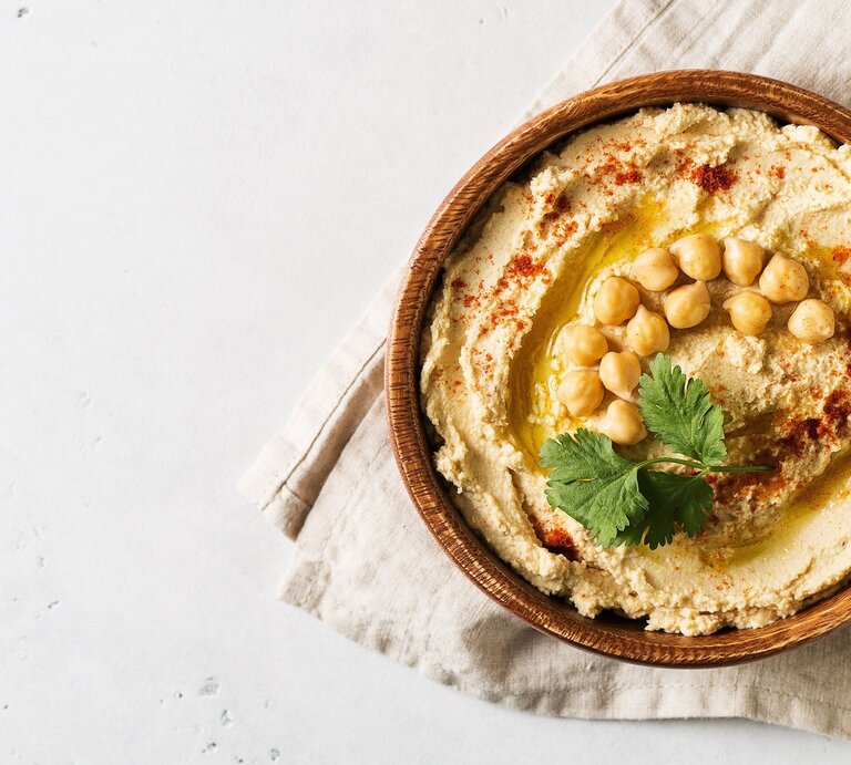 Klassischer Hummus und ganze Kichererbsen in einer runden Schüssel aus Ton / Handtuch / Draufsicht | © EAT CLUB / Isabelle Triemer