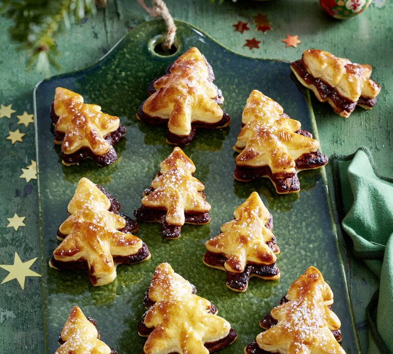 Schräge Draufsicht auf ein Blech mit frisch gebackenen Nougat-Tannenbäume vor einer weihnachtlichen Kulisse. | © EAT CLUB / Isabell Triemer