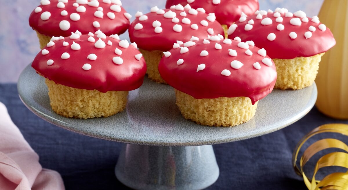 Frontalansicht von sechs Glückspilz-Muffins auf einer Etagere und einem auf einer vergoldeten Untertasse.
