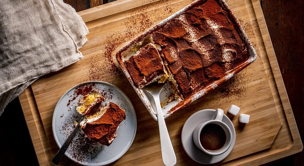 Draufsicht auf eine Auflaufform mit Tirmaisu, daneben ein teller mit einem Stück des italienischen Desserts.