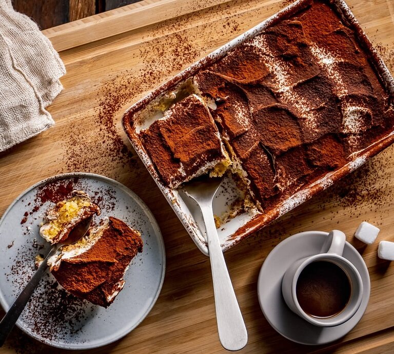 Draufsicht auf eine Auflaufform mit Tirmaisu, daneben ein teller mit einem Stück des italienischen Desserts. | © Getty Images