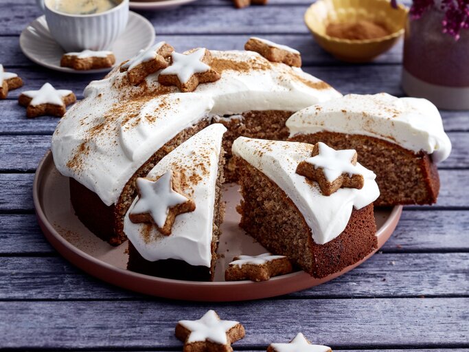Zimtstern-Nusskuchen auf einem braunen Teller auf grauem Hintergrund. Links hinten auf dem Foto eine Tasse Kaffee. | © EAT CLUB / Isabell Triemer
