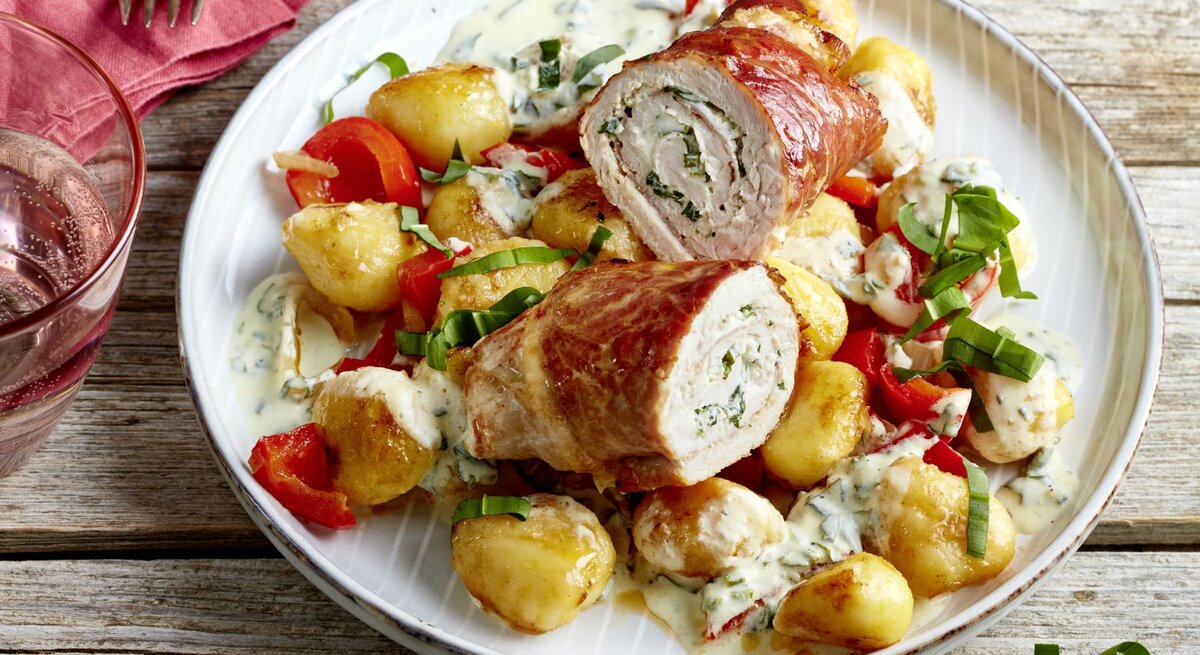 Bärlauch-Schnitzelröllchen auf einem weißen Teller auf hölzernem Hintergrund. 