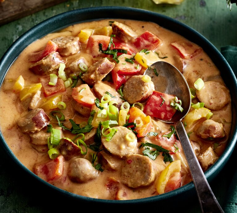 Wurstgulasch mit Paprika-Frischkäse-Soße in einer Schüssel auf dunkelgrünem Hintergrund.  | © EAT CLUB/Isabell Triemer