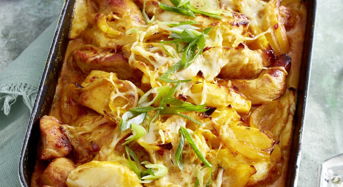 Puten-Curry-Auflauf in einer weißen Auflaufform auf grauem Hintergrund. 