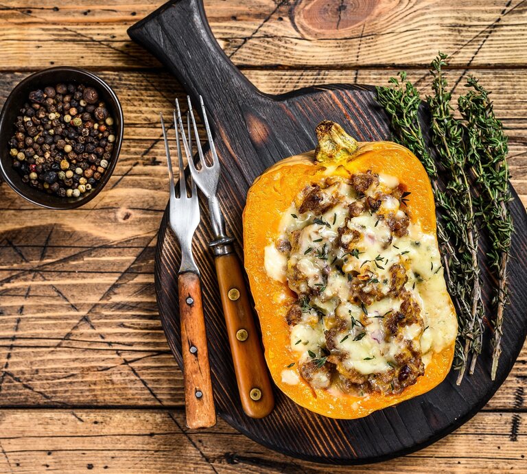 Der gefüllte Kürbis auf einem dunklen Schneidebrett und hellem Holztisch direkt von oben fotografiert. | © stockadobe/ Vladimir
