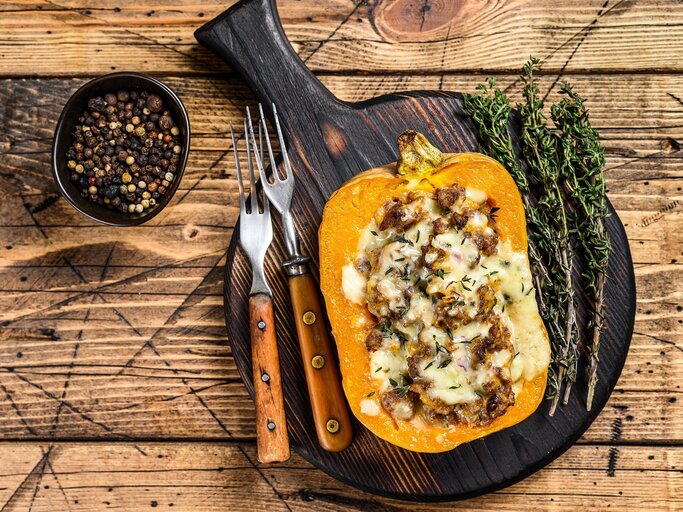 Der gefüllte Kürbis auf einem dunklen Schneidebrett und hellem Holztisch direkt von oben fotografiert. | © stockadobe/ Vladimir