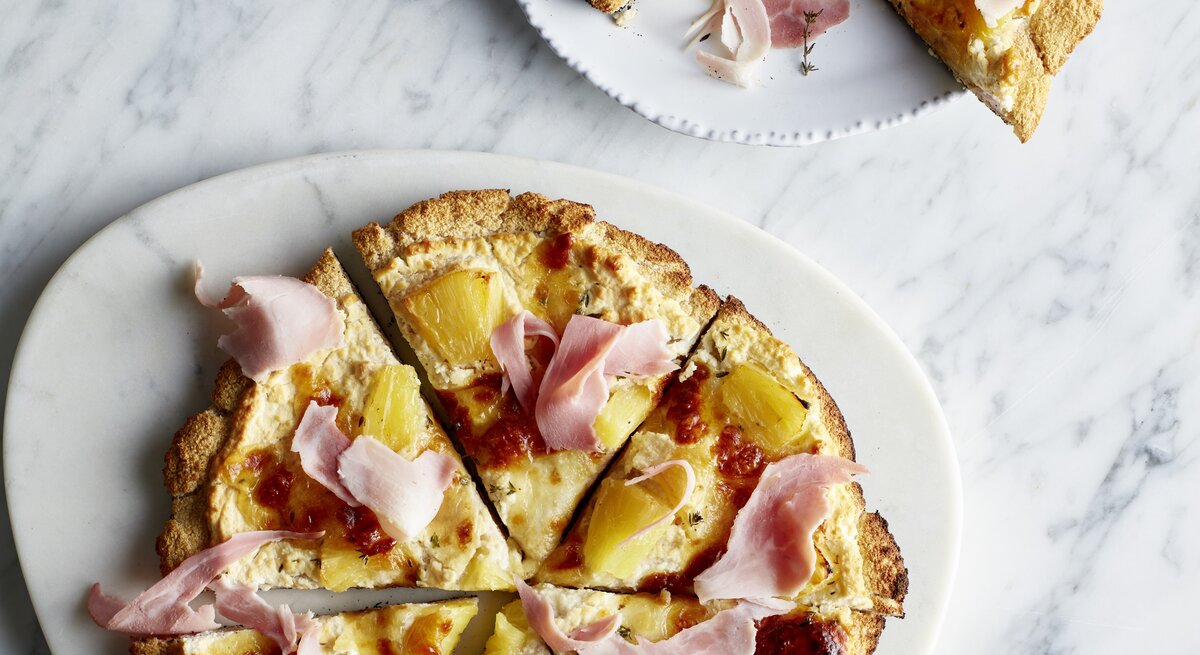 Zwei weiße Teller mit der Low-Carb-Pizza auf hellem Marmoruntergrund direkt von oben fotografiert
