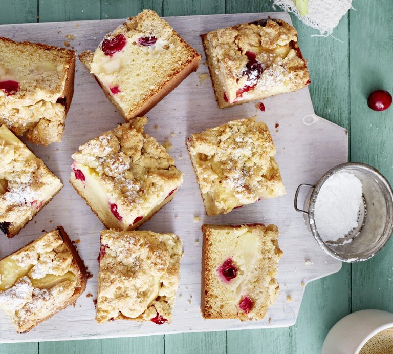 Apfel-Cranberry-Streuselkuchen auf einem weißen Schneidebrett auf grünem Hintergrund. | © EAT CLUB/Isabell Triemer