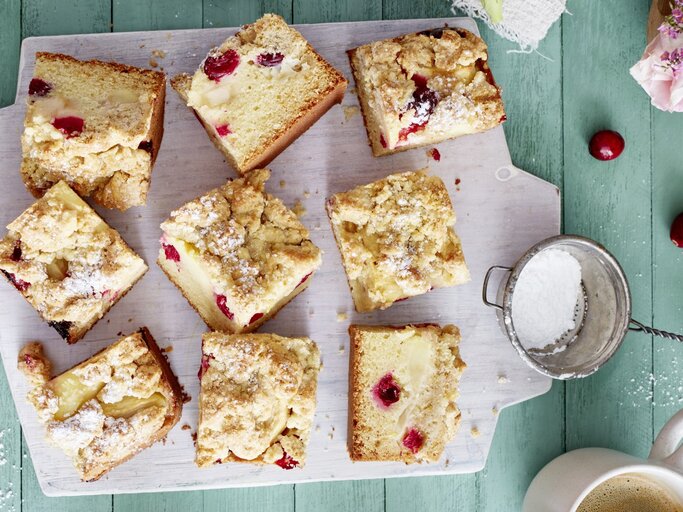 Apfel-Cranberry-Streuselkuchen auf einem weißen Schneidebrett auf grünem Hintergrund. | © EAT CLUB/Isabell Triemer