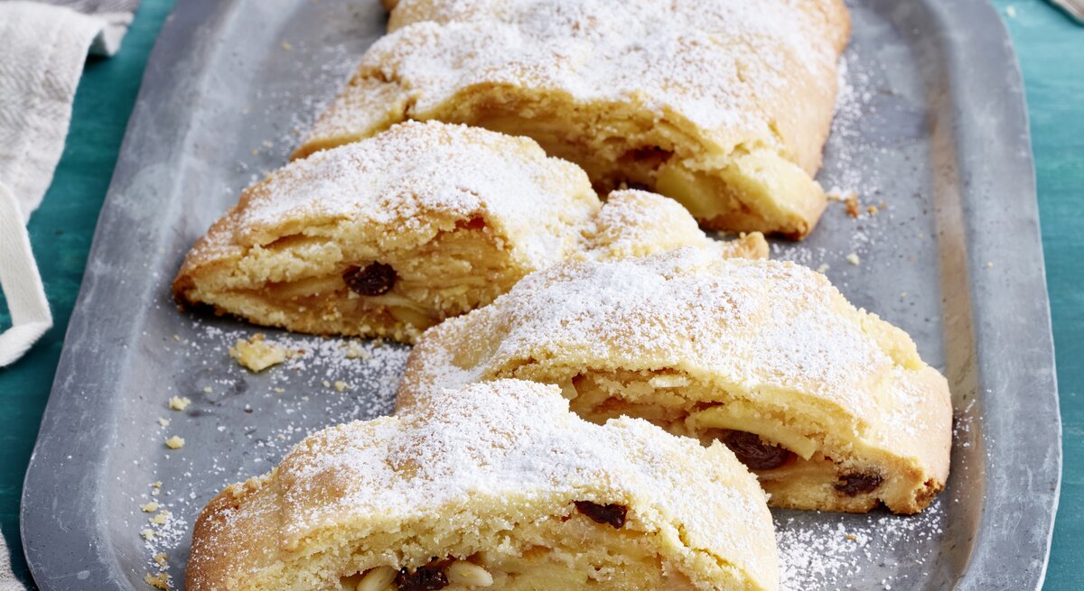 Südtiroler Apfelstrudel auf einem silbernen Servierteller auf blauem Hintergrund. 