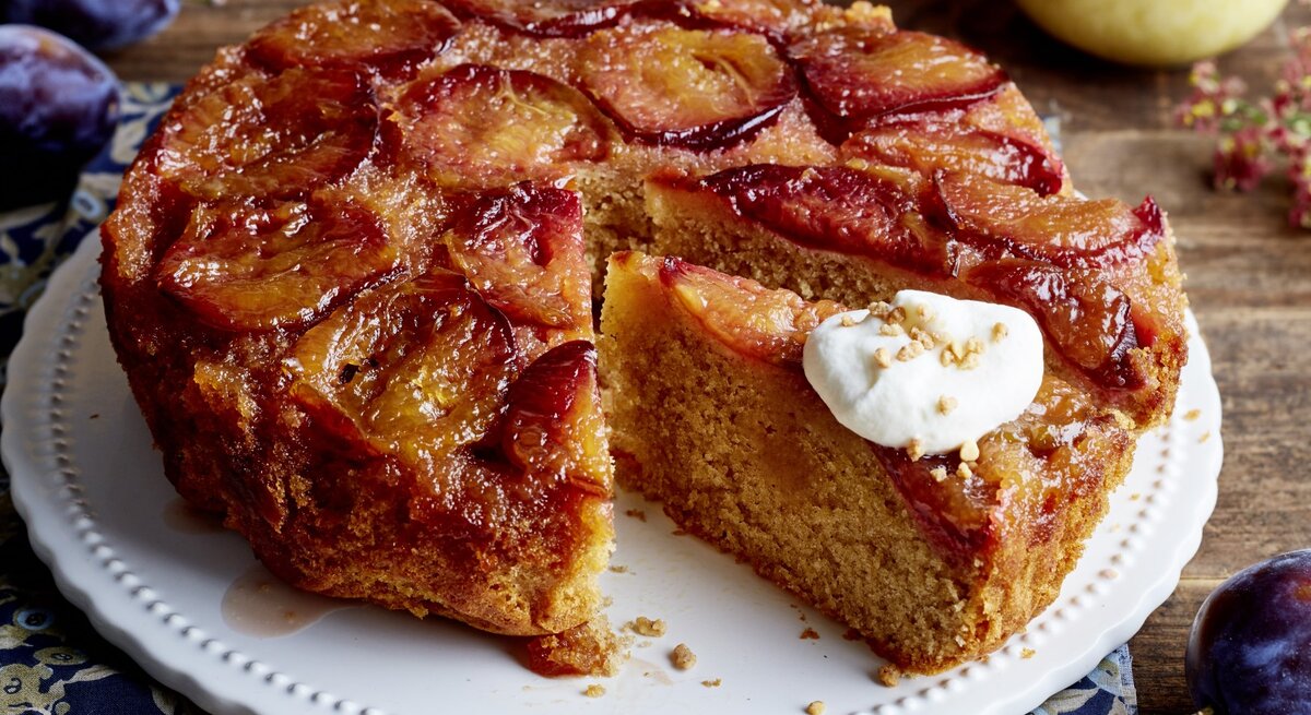 Karamell-Pflaumen-Kuchen auf einem weißen Tortenteller auf hölzernem Hintergrund. 