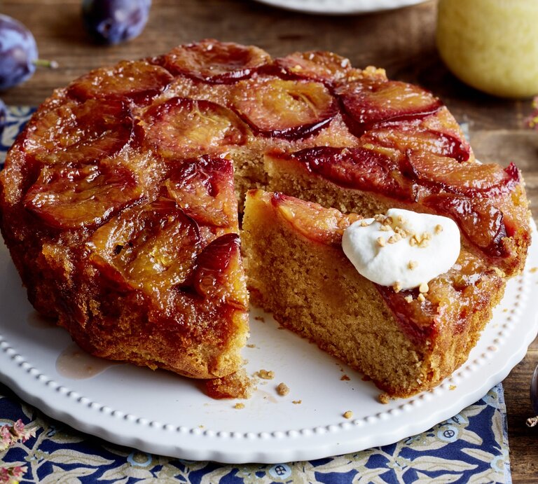 Karamell-Pflaumen-Kuchen auf einem weißen Tortenteller auf hölzernem Hintergrund.  | © EAT CLUB/Isabell Triemer