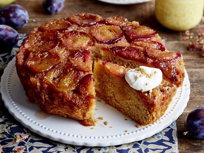 Karamell-Pflaumen-Kuchen auf einem weißen Tortenteller auf hölzernem Hintergrund.  | © EAT CLUB/Isabell Triemer